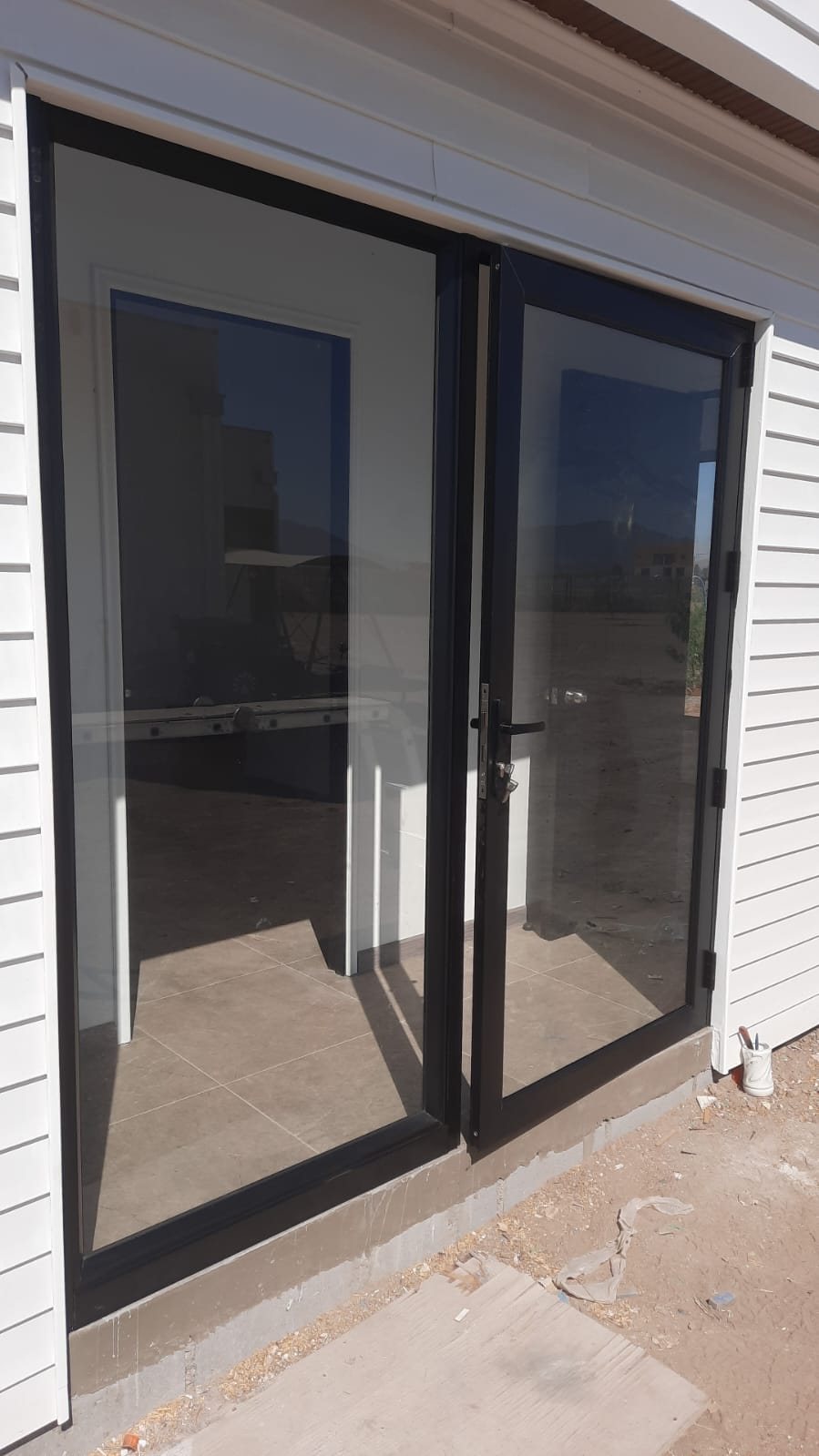 Puerta ventana negra con una hoja abatible y un paño fijo en una casa en construcción